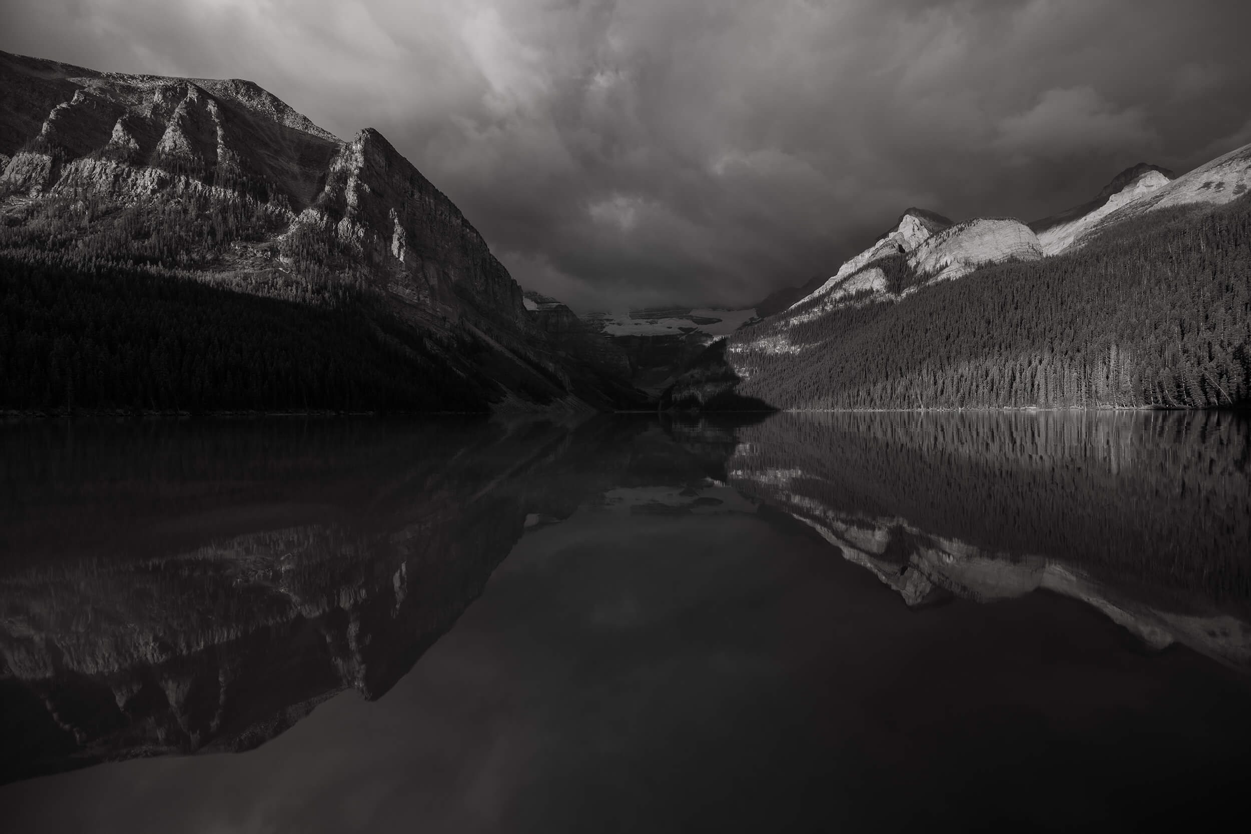 The forest and mountain reflections on the water of Lake Louise on an overcast day.